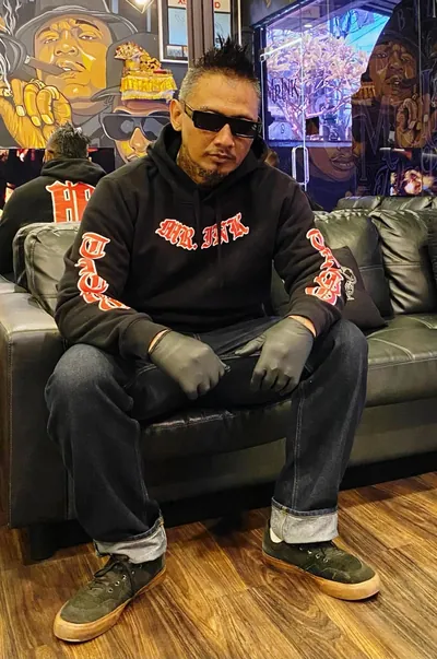 Roy Djihard of Mr Ink Bali in a Mr Ink hoodie, sitting on the couch inside the Seminyak tattoo studio