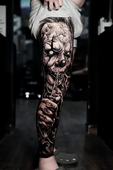 Clown with knife leg sleeve tattoo in black and grey realism at Mr Ink Bali, Seminyak